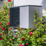outdoor unit of a heat pump heating system surrounded by flowers